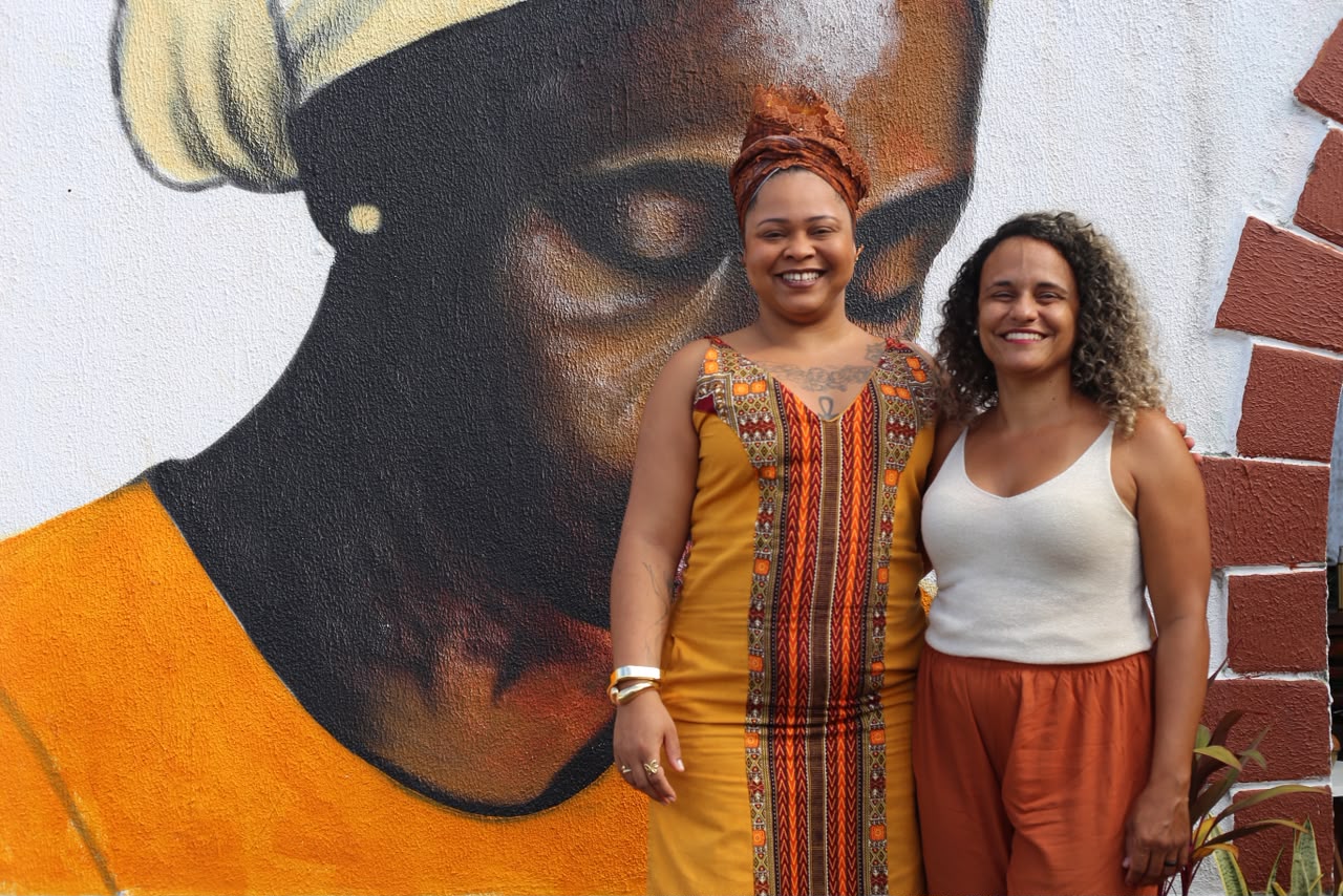 Tayná Passos e Priscila Xavier diante de mural